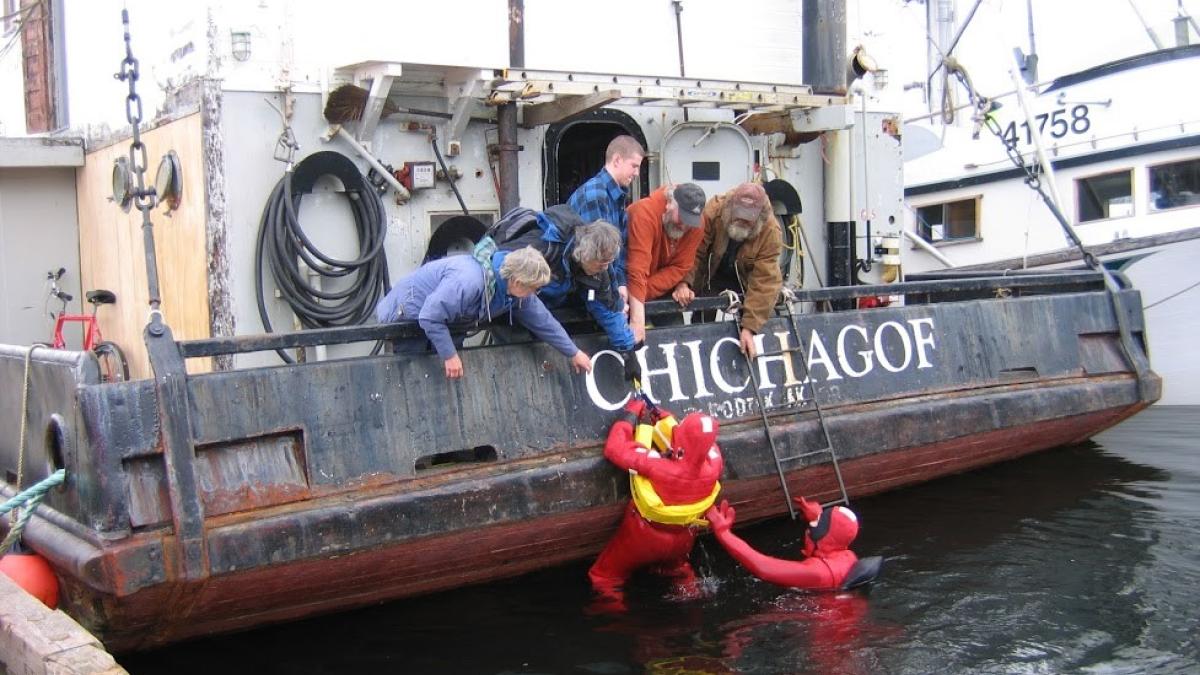 Fishing crew assist person in the water back onto the vessel